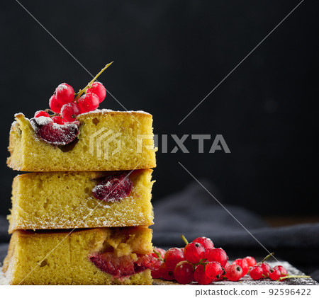 A stack of square slices of baked plum biscuit cake, sprinkled with powdered sugar on top 92596422