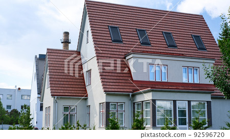 A private house of two floors with triangular roof and an area near the house against a blue sky 92596720