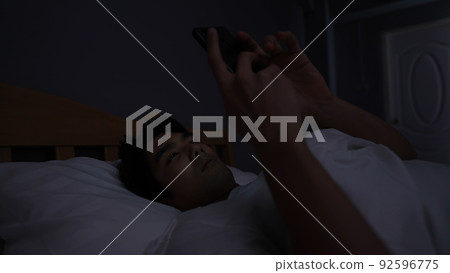 Holiday concept of 4k Resolution. Young Asian man playing mobile phone in bedroom. Holiday concept of 4k Resolution. Young Asian man playing mobile phone in bedroom. 92596775