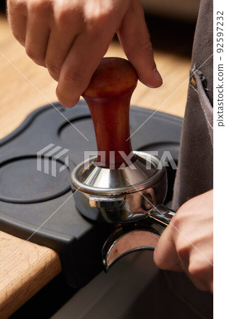 Asian man coffee shop part time employee brew hot coffee in coffee machine. Male barista hand making espresso from ground coffee maker at modern cafe. Small business and part time job working concept. 92597232