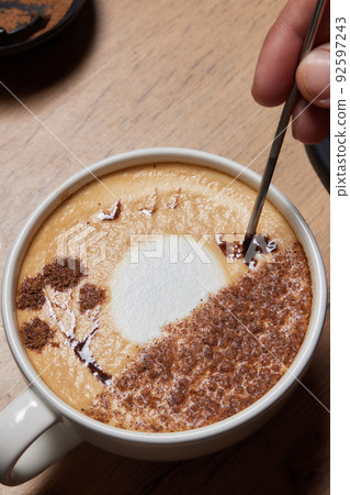 Top view shot of professional barista pouring milk from jar in to a cup of coffee, coffee being prepared by a barista. Focus on hands holding cup of coffee. Top view shot of professional barista pouring milk from jar in to a cup of coffee, coffee being prepared by a barista. Focus on hands holding cup of coffee. 92597243