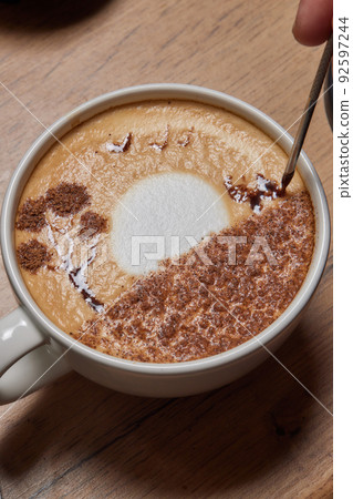 Top view shot of professional barista pouring milk from jar in to a cup of coffee, coffee being prepared by a barista. Focus on hands holding cup of coffee. 92597244