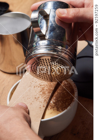 Top view shot of professional barista pouring milk from jar in to a cup of coffee, coffee being prepared by a barista. Focus on hands holding cup of coffee. 92597259