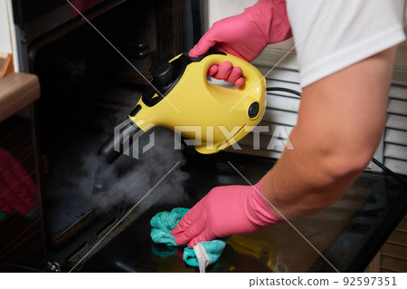 Experienced worker in rubber gloves steam-cleaning kitchen equipment. 92597351