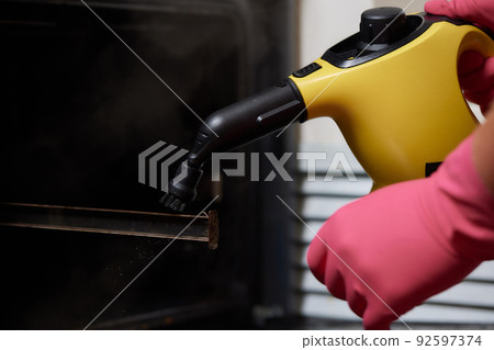 Experienced worker in rubber gloves steam-cleaning kitchen equipment. Experienced worker in rubber gloves steam-cleaning kitchen equipment. 92597374