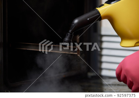 Experienced worker in rubber gloves steam-cleaning kitchen equipment. 92597375