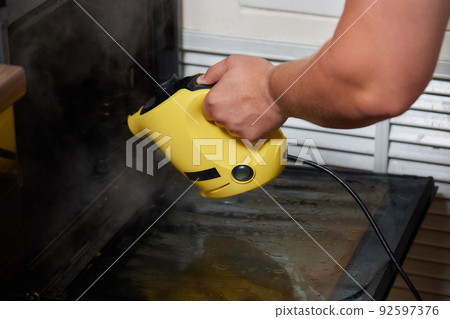 Experienced worker in rubber gloves steam-cleaning kitchen equipment. Experienced worker in rubber gloves steam-cleaning kitchen equipment. 92597376