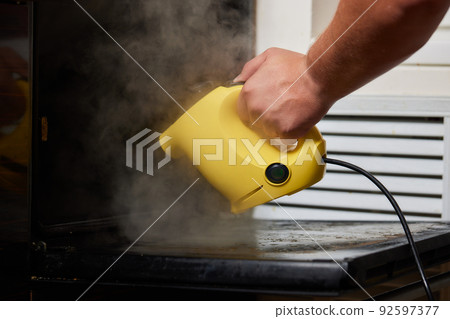Experienced worker in rubber gloves steam-cleaning kitchen equipment. Experienced worker in rubber gloves steam-cleaning kitchen equipment. 92597377