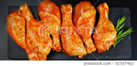 Barbeque marinated chicken dramsticks on a black cooking board on a black background with fresh rosemary leaves. Semi-finished product, Marinated product, quick cooking.Baner. Barbeque marinated chicken dramsticks on a black cooking board on a black background with fresh rosemary leaves. Semi-finished product, Marinated product, quick cooking.Baner. 92597402