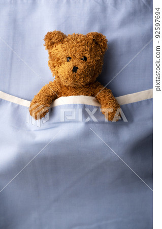 Brown teddy bear laying on blue bed 92597694