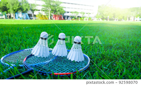 Badminton shuttlecocks on blue raquettes are on green field 92598070