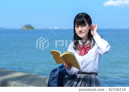 A high school girl reading a book while sitting on a beautiful seaside breakwater, studying, novel, after school, at the beach 92598316
