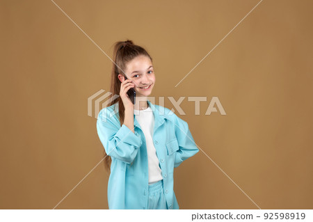 A beautiful smiling teenage girl is standing and talking on the phone 92598919
