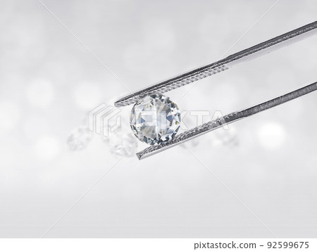 Dazzling diamond held in diamond tweezers in front of a white background, reflections on the ground. Lot of copyspace 92599675