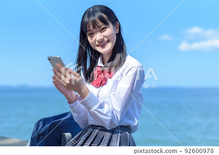 高中女生應用 SNS 海邊樂趣互聯網坐在美麗的海濱防波堤上,使用智能手機 高中女生應用 SNS 海邊樂趣互聯網坐在美麗的海濱防波堤上,使用智能手機 92600978