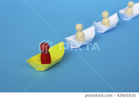 Leadership Concept - Red wooden figure on yellow paper ship origami leading the rest of the figure on white paper ship. Leadership Concept - Red wooden figure on yellow paper ship origami leading the rest of the figure on white paper ship. 92601610