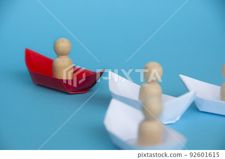 Leadership Concept - Wooden figure on red paper ship origami leading the rest of the figure on white paper ship. Leadership Concept - Wooden figure on red paper ship origami leading the rest of the figure on white paper ship. 92601615