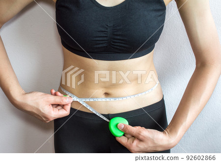 Sportswoman measuring her waist by measure tape after hard workout isolated on white wall background. Sportswoman measuring her waist by measure tape after hard workout isolated on white wall background. 92602866