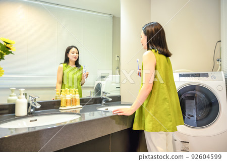 A young woman brushing her teeth in a double-sink dressing room A young woman brushing her teeth in a double-sink dressing room 92604599