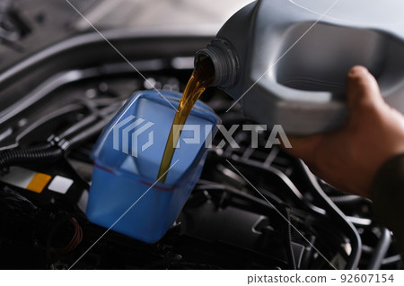 Auto mechanic replaces and pours fresh oil into engine at service station 92607154