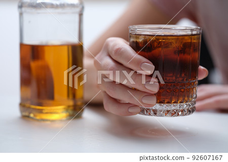 Woman hand holds glass of whiskey or cognac with bottle Woman hand holds glass of whiskey or cognac with bottle 92607167
