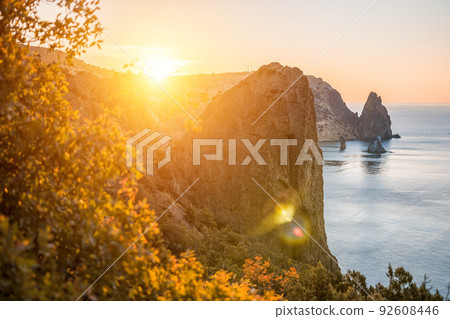 Selective focus. Autumn foliage and sea landscape with warm sunset light over a rocky coastline Calm sea on a background of rocky shores. The concept of an ideal place for autumn travel and relaxation 92608446