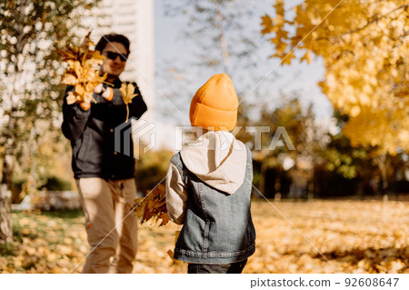 Father and son having fun in autumn park with fallen leaves, throwing up leaf. Child kid boy and his dad outdoors playing with maple leaves. 92608647
