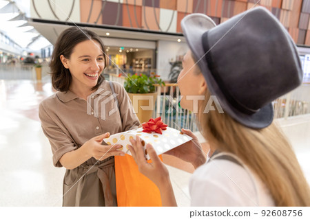 Young woman presenting gift to her female friend in mall 92608756