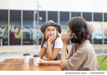 Pretty young girl wearing hat drinking coffee with her friend 92608908