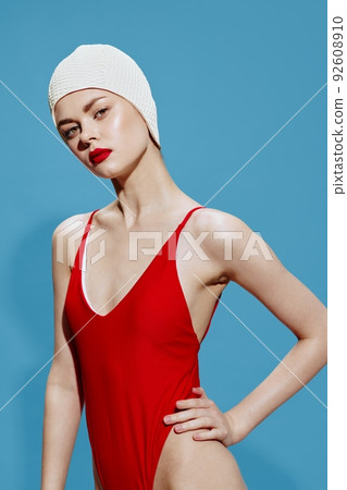 Charming woman in a red swimsuit bathing cap posing holding her hand on her waist on a blue background. Conceptual pop art 92608910