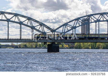 The train rides on the railway bridge against the background of a cloudy blue sky. 92610766