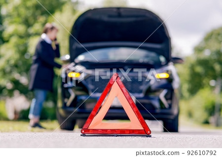 Red emergency stop sign and woman talking on the phone near a broken car on the road Red emergency stop sign and woman talking on the phone near a broken car on the road 92610792