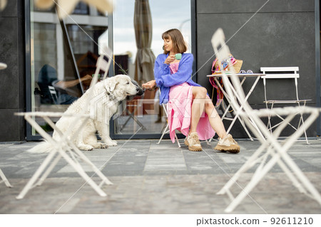 Woman sits with her adorable white dog at cafe on a street 92611210