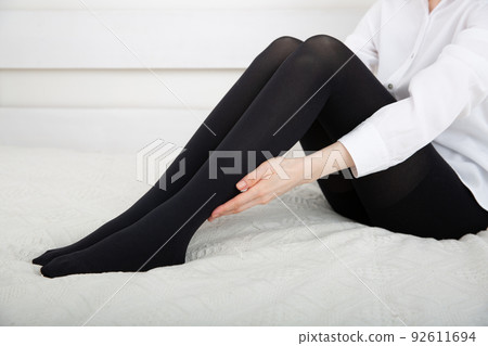Beautiful long female legs in stockings. Girl putting on stockings at home in a white room. Black tights. Varicose veins prevention. Woman body in underwear. Beautiful long female legs in stockings. Girl putting on stockings at home in a white room. Black tights. Varicose veins prevention. Woman body in underwear. 92611694