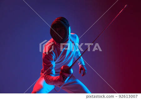Male fencer with smallsword practicing fencing isolated on purple background in neon light. Sport, energy, skills, achievements 92613007