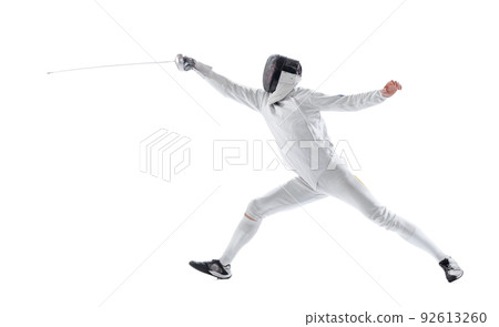 Dynamic portrait of young man, fencer in in fencing costume with sword in hand training isolated on white studio background. Sport, energy, skills 92613260