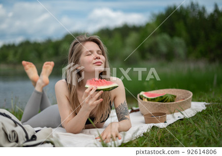 Girl relaxing and eat watermelon outdoor near lake. Picnic in nature Girl relaxing and eat watermelon outdoor near lake. Picnic in nature 92614806