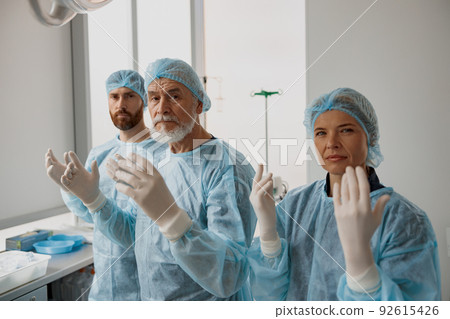 Team of surgeons in the operating room ready for surgery in clinic looking at camera Team of surgeons in the operating room ready for surgery in clinic looking at camera 92615426