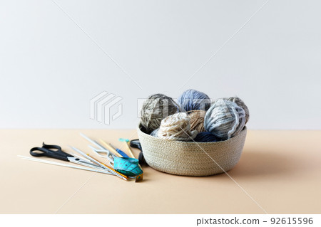 Gray and blue balls of thread in a beige basket with knitting needles for knitting warm clothes with scissors and a centimeter Gray and blue balls of thread in a beige basket with knitting needles for knitting warm clothes with scissors and a centimeter 92615596