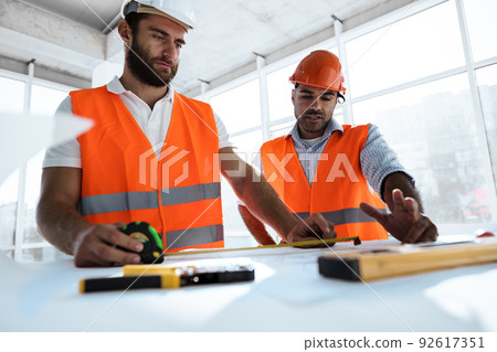 Two engineers man looking at project plan on the table in construction site 92617351