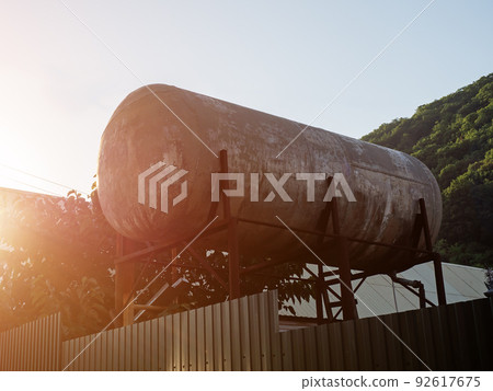 Large iron water tank behind the fence. A large water tank on rusty iron supports stands in a private yard. Solar water heater on props. Alternative energy and ecology 92617675