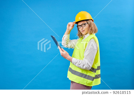 Business woman builder working with tablet PC. Smiling woman in studio on blue background. The concept of construction, repair, decoration. Studio shooting Business woman builder working with tablet PC. Smiling woman in studio on blue background. The concept of construction, repair, decoration. Studio shooting 92618515
