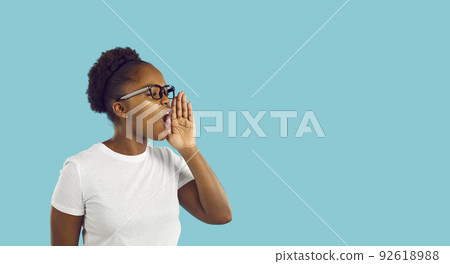 African American woman talking or shouting with hand at mouth on blue copy space background African American woman talking or shouting with hand at mouth on blue copy space background 92618988