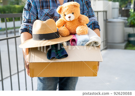 Holding clothing donation box with used clothes and doll at home to support help for poor people in the world. Holding clothing donation box with used clothes and doll at home to support help for poor people in the world. 92620088