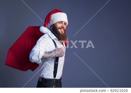 Smiling bearded man in Santa's hat carries big sack with presents. Christmas sales. New Year concept Smiling bearded man in Santa's hat carries big sack with presents. Christmas sales. New Year concept 92621026