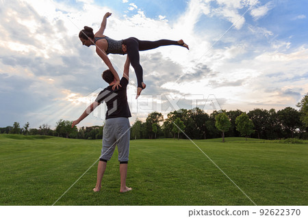 Healthy young man holds in the air a woman balancing and doing acro yoga Healthy young man holds in the air a woman balancing and doing acro yoga 92622370