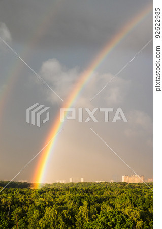 bright rainbow in gray blue sky over sunlit park bright rainbow in gray blue sky over sunlit park 92622985