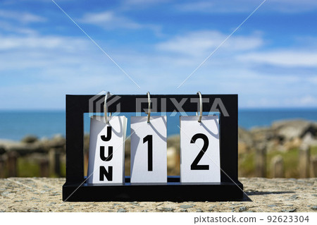 Jun 12 calendar date text on wooden frame with blurred background of ocean. Jun 12 calendar date text on wooden frame with blurred background of ocean. 92623304