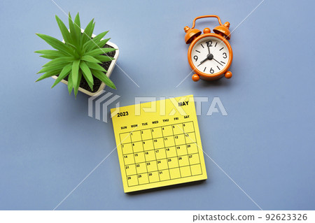 May 2023 calendar on adhesive note with alarm clock set at 8 o'clock. 92623326