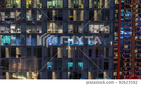 Night aerial view of office or apartment building glass window facade with illuminated lighted workspace rooms timelapse. 92623582
